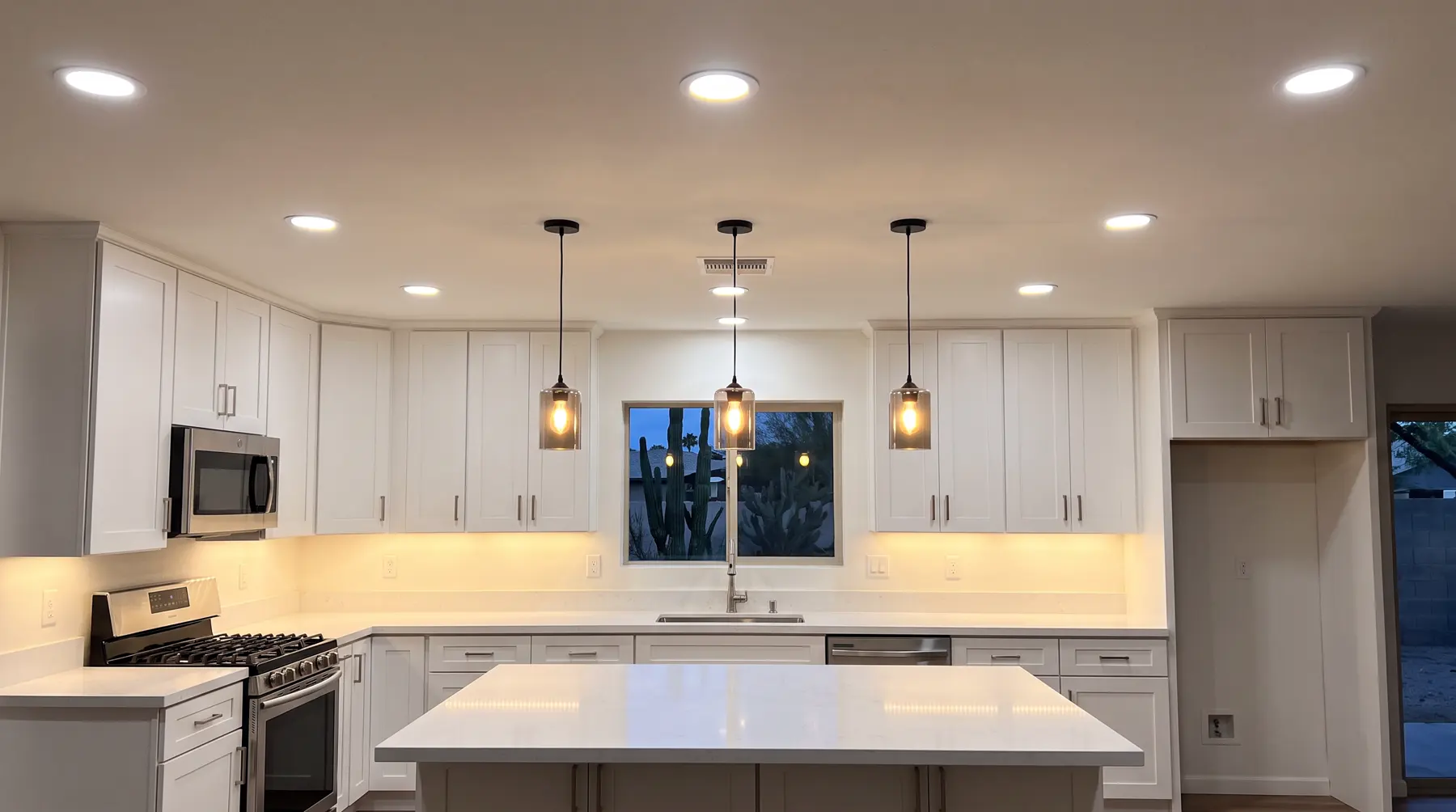 A white kitchen with recessed lights, pendants over the island and glowing under-cabinet lights